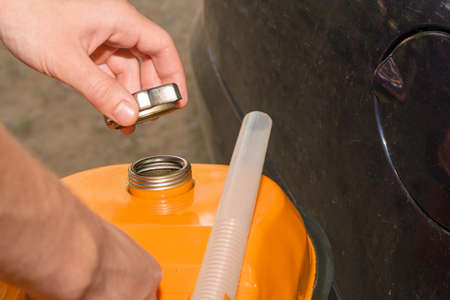 a man holds an orange gasoline canister in his hand next to the car unscrews the cork from the filler neck. High quality photoの写真素材
