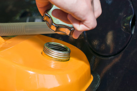 a man holds an orange gasoline canister in his hand next to the car unscrews the cork from the...