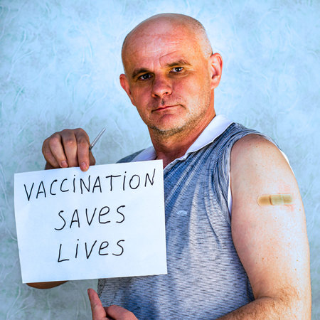 a bald middle-aged man with a plaster on his arm holds a sheet with the inscription vaccination...