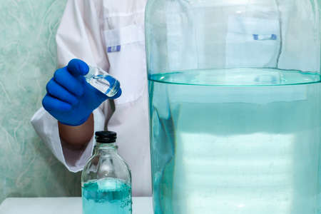 a medical worker in the laboratory holds a bottle of poison liquid in his hand there are other vessels of different sizes on the table. High quality photoの写真素材