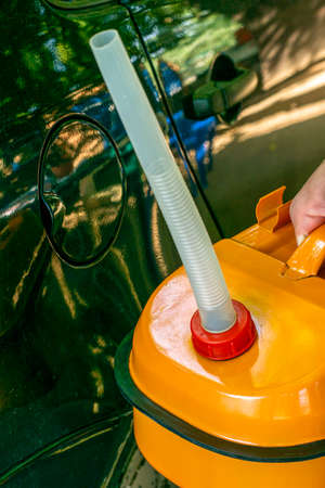a man holds an orange canister of gasoline in his hand next to the car and screws a drain hose on the neckの写真素材