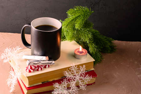 a New Year's card a cup of coffee on the books next to a candle chocolates Christmas candies snowflakes and fir twigs. High quality photoの写真素材