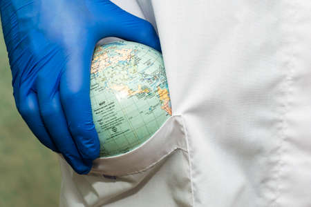 a doctor in a white coat and blue gloves puts a globe of the globe concept healthcare pharmaceuticals in the pocket of his robe. High quality photoの写真素材