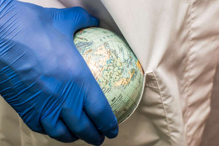 a doctor in a white coat and blue gloves puts a globe of the globe concept healthcare pharmaceuticals in the pocket of his robe. High quality photoの写真素材