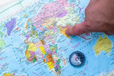 a person points a finger at a place on a geographical map next to a compass a concept of travel...