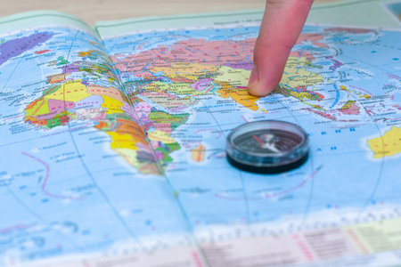 a person points a finger at a place on a geographical map next to a compass a concept of travel...