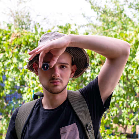 a young tourist guy holds a compass with his hand instead of an eye the concept of tourism travel. High quality photoの写真素材