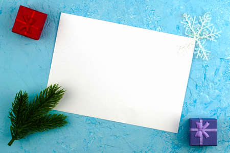 a white sheet on a blue surface in a frame of green spruce twigs gift boxes and snowflakes a conceptual letter to Santa Claus with New Year's wishes. High quality photoの写真素材