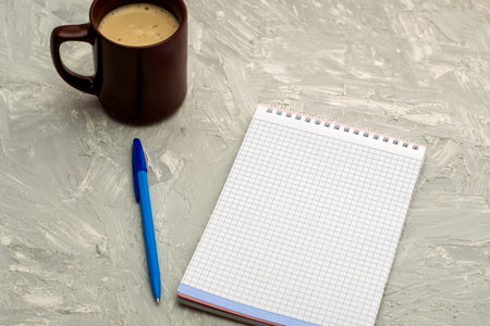 a cup of cappuccino coffee a notepad and a fountain pen on a gray surface. High quality photo