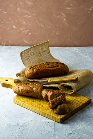 two fresh rye buns on a cutting wooden board and a piece of burlap one of the buns is cut there is a...