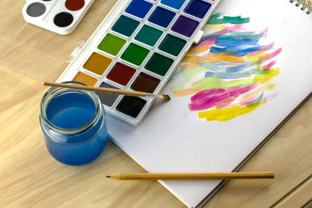 watercolor paints a brush a jar of water and a pencil on a white sheet with paint samples. High quality photoの写真素材