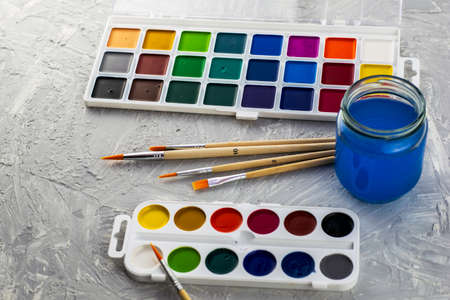 watercolor paints brushes and a jar of water on a gray surface. High quality photoの写真素材