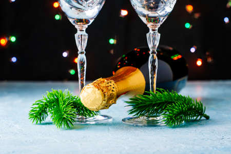 a bottle of champagne and two glass glasses with fir twigs on legs on a black background with lights. High quality photoの写真素材
