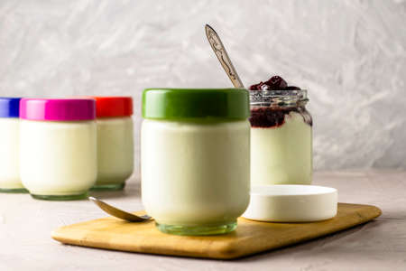 a jar of yogurt with cherry jam on a cutting board next to other jars of yogurt. High quality photoの写真素材