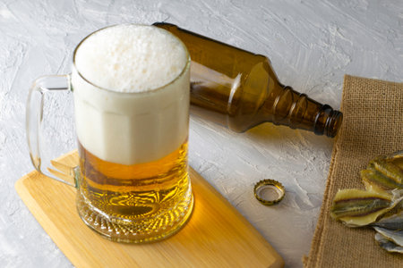 a glass of beer, an empty beer bottle, a cork and dried fish on burlap. High quality photo
