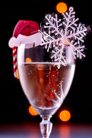 a glass of champagne with a decoration in the form of a Santa Claus hat, a caramel cane and snowflakes on a black background with a backlit close-up. High quality photoの写真素材
