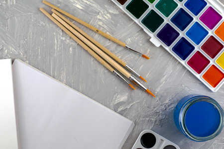 watercolor paints brushes a jar of water and a sheet of white paper on a gray surface. High quality photoの写真素材