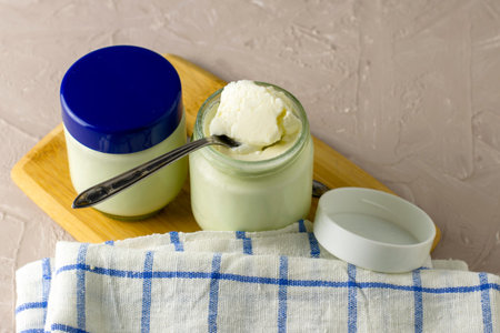 cans of homemade yogurt and spoons on a cutting board next to a kitchen towel. High quality photo