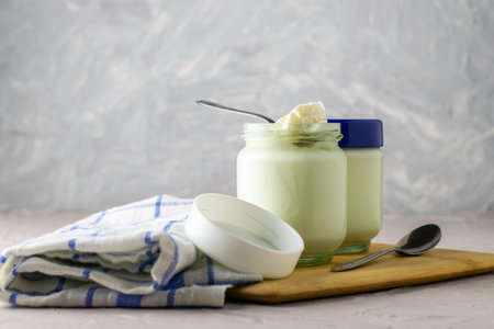 cans of homemade yogurt and spoons on a cutting board next to a kitchen towel. High quality photoの写真素材