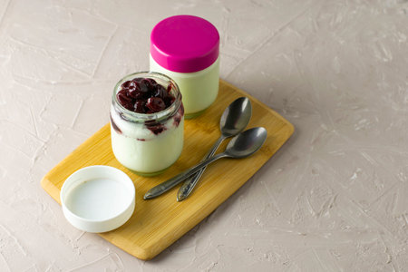 a jar of yogurt with cherry jam on a cutting board next to other jars of yogurt. High quality photoの写真素材