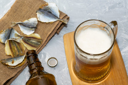 a glass of beer, an empty beer bottle, a cork and dried fish on burlap. High quality photo