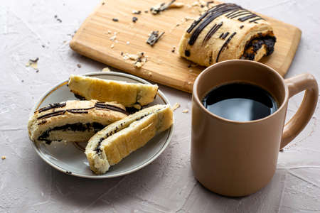 a cup of coffee and a sliced puff pastry bun with poppy seeds and chocolate on a cutting board and on a plate. High quality photoの写真素材