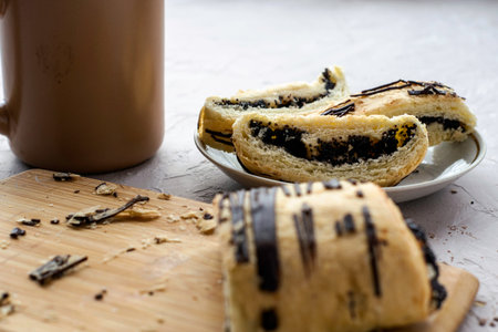 a cup of coffee and a sliced puff pastry bun with poppy seeds and chocolate on a cutting board and...