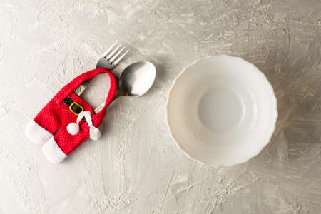 spoon and fork in a package in the form of a fur coat and Santa Claus pants next to a plate on the table with copyspace. High quality photoの写真素材