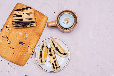sliced puff pastry bun with poppy seeds and chocolate on a cutting board and on a saucer and a coffee mug top view copy space. high quality photoの写真素材