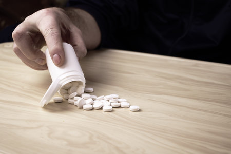 a man pours pills out of a plastic bottle on the tableの写真素材