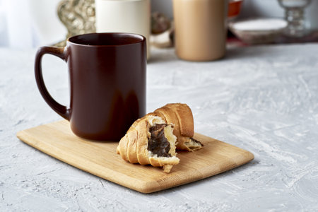 a coffee mug and a croissant broken in half on a cutting board