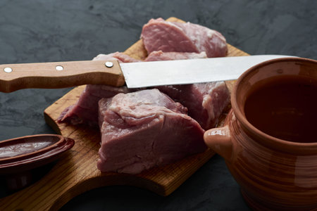 a piece of meat cut into pieces on a chopping board, a pot for chanakhi and a knife next to it. high quality photoの写真素材