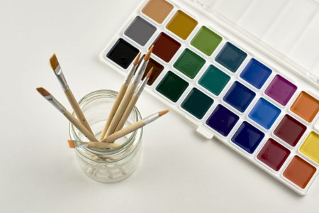 watercolor paints and a jar with brushes for painting on a white surface. high quality photoの写真素材