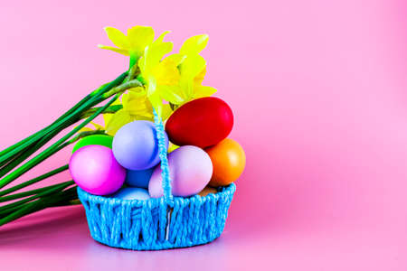 colorful Easter eggs in a basket and a bouquet of flowers on a pink background. high quality photoの写真素材