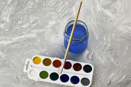 watercolor paints a paint brush and a jar of water on a gray surface. high quality photo