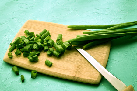 sliced green onions on a wooden chopping board next to a knife. high quality photo