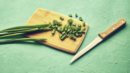 sliced green onions on a wooden chopping board next to a knife. high quality photo