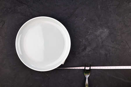 a plate wrapped with a centimeter and a fork on a black background with a copy space concept diet nutrition. high quality photoの写真素材