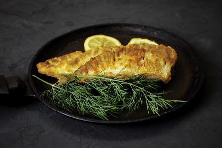fried fish with lemon and herbs in a frying pan on the table. high quality photoの写真素材