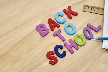 the phrase back to school is laid out in multicolored letters on the table next to a pencil ruler...