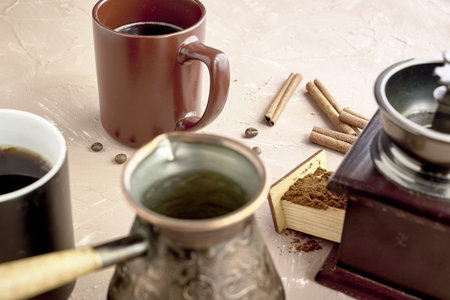 coffee grinder two mugs of cinnamon coffee beans and a turk for brewing coffee on the table. high...