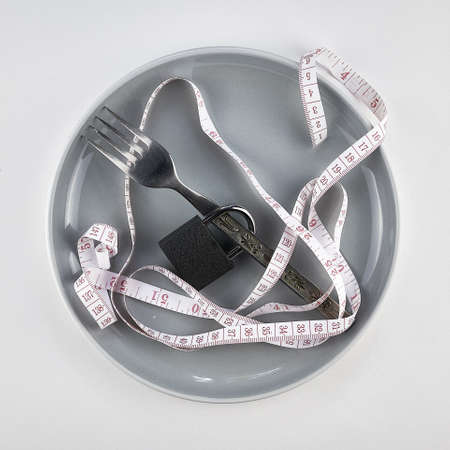 concept diet proper nutrition on a plate fork with lock and measuring tape. high quality photoの写真素材