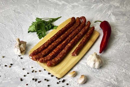 spicy smoked sausages on a cutting board next to red pepper garlic spices and herbs on the table. high quality photoの写真素材