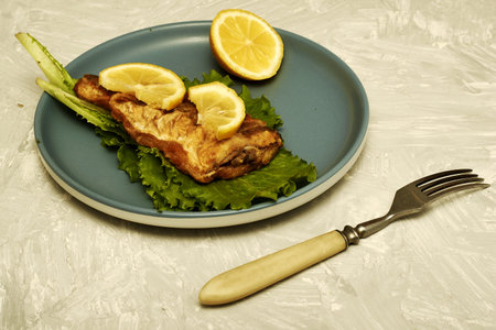 fried fish with lemon and herbs on a plate and a fork on the table. high quality photoの写真素材