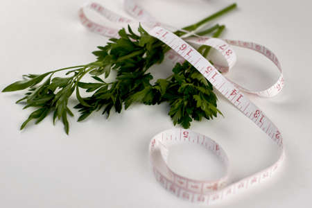 green parsley leaves wrapped with measuring tape on a white background concept diet vegetarianism. high quality photoの写真素材