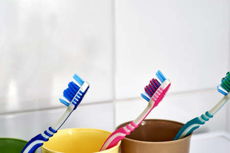 three colorful toothbrushes in colorful mugs on the bathroom table. high quality photoの写真素材