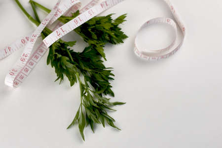 green parsley leaves wrapped with measuring tape on a white background concept diet vegetarianism. high quality photoの写真素材