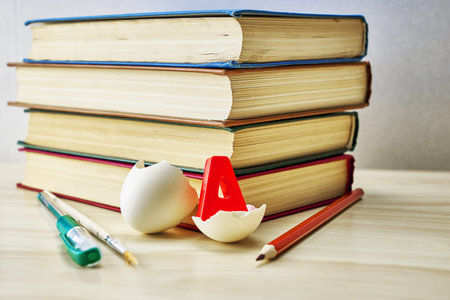 a stack of books writing materials and a split chicken egg with the letter a inside on the table...