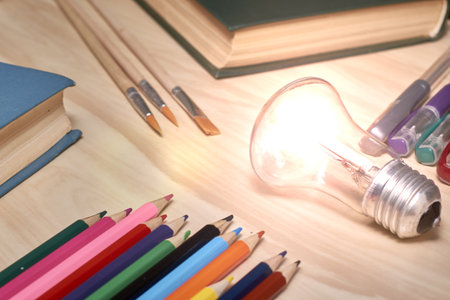fountain pens pencils brushes books and a burning light symbolizing knowledge on the table concept...