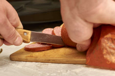 a man prepares sandwiches in a sandwich maker cuts sausage with a knife on a wooden cutting board. high quality photoの写真素材